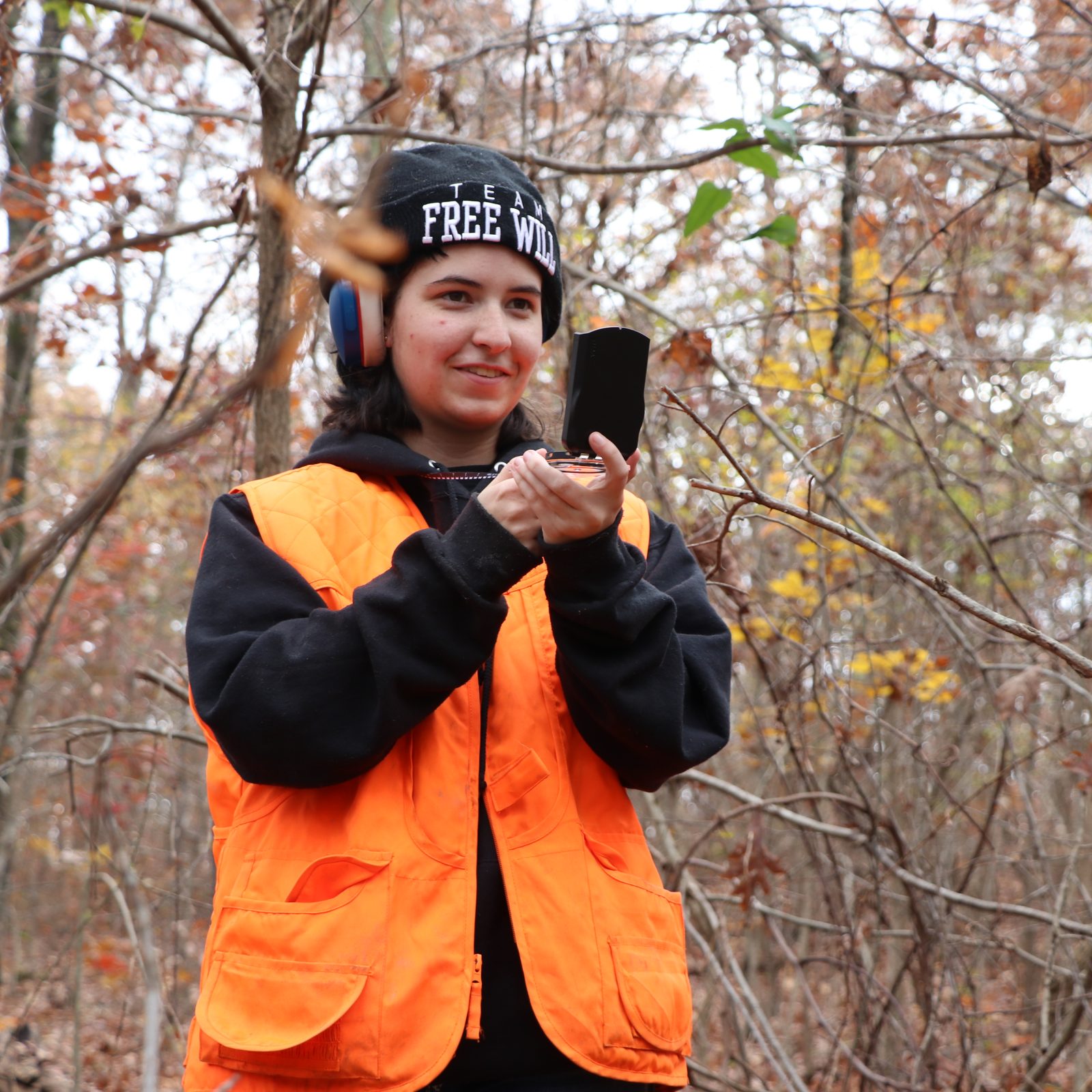 female student wearing orange safety vest in forest taking measurements